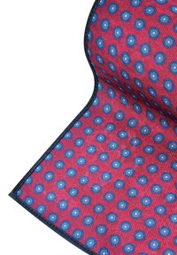 Tekstylny dywanik z czerwoną bazą, w którym znajduje się wzór niebieskich okręgów z jaśniejszymi niebieskimi środkami. Krawędzie wykończone ciemnoniebieskim kolorem, teksturowana powierzchnia.