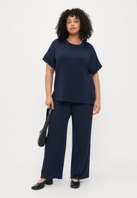 Ναυτικό μπλε τοπ κοντό μανίκι με άνετη εφαρμογή, συνδυασμένο με παντελόνια φαρδιάς γραμμής, και τα δύο φτιαγμένα από μαλακό ύφασμα. Μαύρη τσάντα με αξεσουάρ από καρφιά.