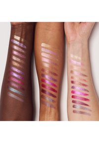Tre arme med øjenskygge swatches i forskellige nuancer, herunder metalfaver og matte, der spænder fra gyldne og pink til lilla og blå.