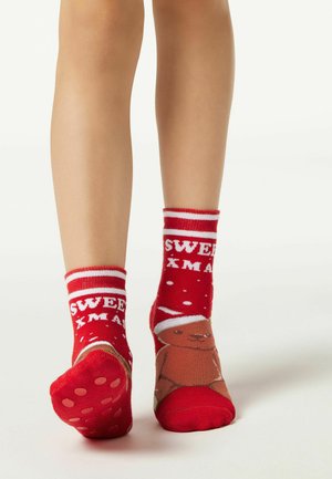 Röda strumpor med vita randiga mudd, med en design av en pepparkaksgubbe och texten "SÖT JUL". Texturerade sulor har prickar.