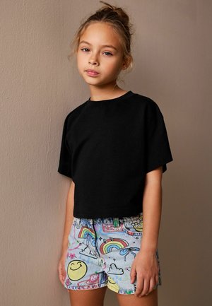 Sort croppet t-shirt kombineret med multifarvede denimshorts, der har smiley-ansigter, regnbuer og skyer i et legende mønster.