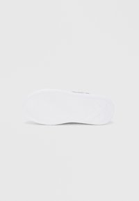 Λευκό αθλητικό παπούτσι με υφασμένη λαστιχένια σόλα που έχει κυματιστό σχέδιο, επίπεδο σχέδιο και ελάχιστη σήμανση.