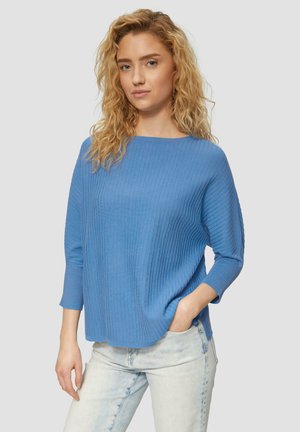Pull en maille côtelée bleu clair avec un col bateau et des manches trois-quarts, associé à un jean en denim clair. La texture semble douce et lisse.