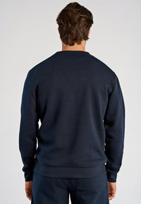 Felpa blu navy in misto cotone, design con scollo rotondo, polsini e orlo a coste, texture liscia, marchio minimale, con silhouette aderente.