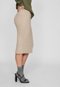 Stickad beige midi kjol med vertikal ribbning, kombinerad med grå ankelsockor och svarta remmar med klacksandaler, visad från en sida.