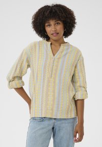 Chemise à boutons fabriquée dans un tissu texturé, avec des rayures verticales jaunes et bleues, dotée d'un col montant et de manches retroussées.