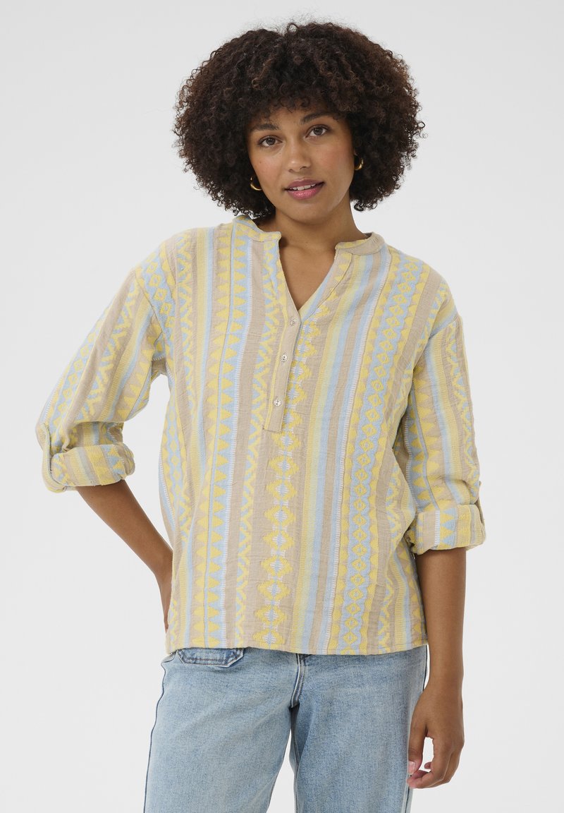 Chemise à boutons fabriquée dans un tissu texturé, avec des rayures verticales jaunes et bleues, dotée d'un col montant et de manches retroussées.