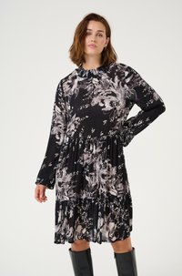 Musta kukallinen mekko pitkillä hihoilla, laskostetusta kankaasta ja röyhelöhelmasta. Sisältää harmaita ja valkoisia kukkakuvioita tummalla taustalla.