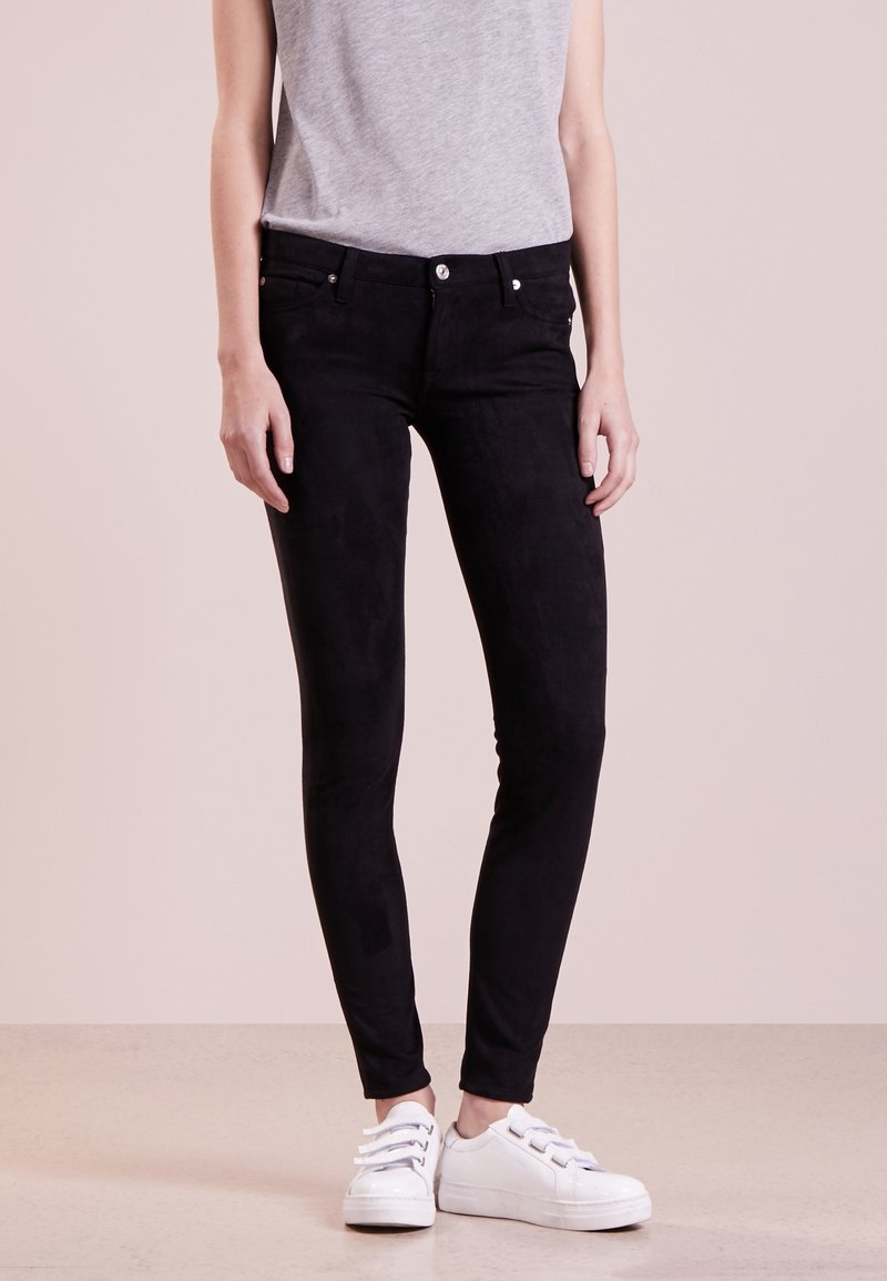Černé semišové skinny džíny se slim fit střih a designem s pěti kapsami, spárované s bílými šněrovacími teniskami a šedým topem bez rukávů.