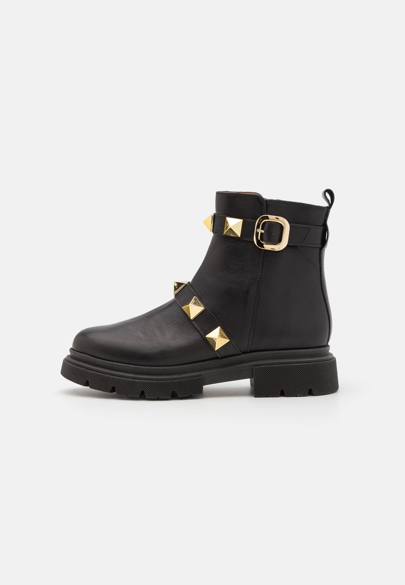 Botine negre din piele, cu ț studs piramidale aurii și accente cu cataramă, având o talpă groasă din cauciuc texturat și un cârlig pe călcâi.