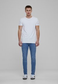 Fehér, kerek nyakú póló világoskék, slim-fit farmernadrággal párosítva. A farmernadrág kopott részletekkel rendelkezik. Fehér és szürke sportcipőt visel.