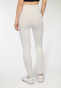 Jasnoszare legginsy z wysokim stanem, o gładkiej, elastycznej fakturze i dopasowanym kroju. Połączone z białymi butami sportowymi.
