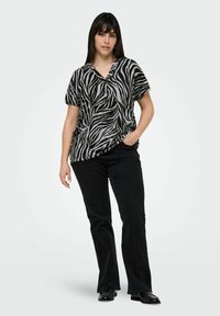 Svart och vit randig kortärmad topp med V-ringning, ihopparad med svarta utsvängda jeans. Modellen står med en hand i fickan.