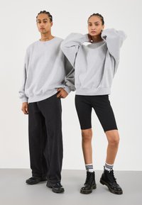 Due modelli indossano felpe grigie oversize. Il modello maschile le abbina a pantaloni larghi neri; il modello femminile indossa pantaloncini da bici neri e stivali.