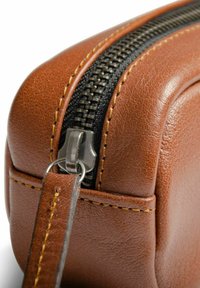 Hnedá kožená taška s textúrovaným povrchom, vybavená čiernym zipsom a kovovým ťaháčikom. Žlté šitie pozdĺž okrajov pridáva na detailoch.