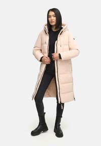 Light pink puffer coat with a hood, featuring a front zipper, black accents, and quilted design, worn over a black top and jeans.