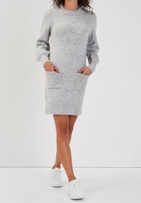 Robe tricotée grise avec un col rond, des manches longues, des poignets côtelés et deux poches avant. Présente un motif décoratif sur le corsage.