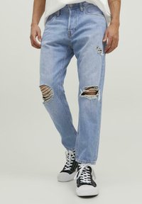 Jeans rasgados de color azul claro con desgastes en las zonas de las rodillas, con un corte relajado y diseño clásico de cinco bolsillos, combinados con zapatillas negras.