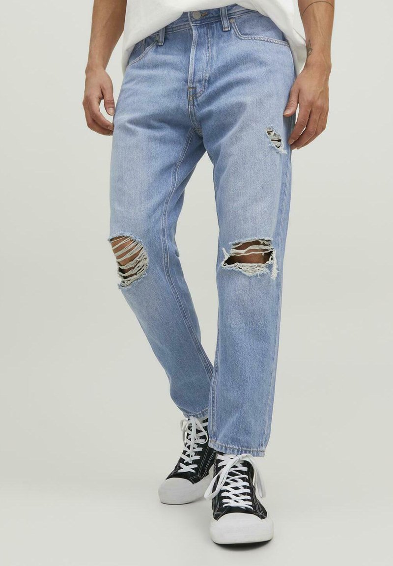 Jeans rasgados de color azul claro con desgastes en las zonas de las rodillas, con un corte relajado y diseño clásico de cinco bolsillos, combinados con zapatillas negras.
