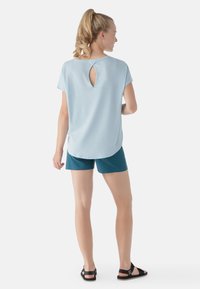 Top corto azzurro con maniche corte e dettaglio a chiave sul retro, abbinato a pantaloni corti turchesi e sandali neri, caratterizzato da una vestibilità comoda e un tessuto morbido.