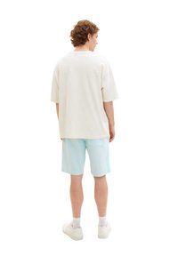 Light beige oversized t-shirt and light blue shorts. T-shirt features short sleeves; shorts are knee-length with a back pocket. White sneakers.