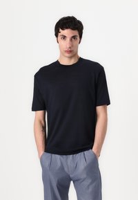 T-shirt bleu marine à manches courtes avec un col rond, fabriqué en tissu léger, associé à un pantalon plissé gris clair.