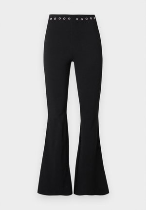 Pantalon noir taille haute ajusté avec des œillets métalliques sur la ceinture et des jambes évasées.