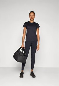 Svart atletisk T-skjorte og tettsittende leggings, begge i fukttransporterende stoff. Hun bærer en svart duffelbag og har på seg svarte joggesko.