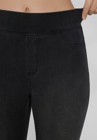 Pantalones de mezclilla negros de talle alto con una textura suave, que presentan detalles cosidos, un bolsillo frontal y una cinturilla flexible para mayor comodidad.