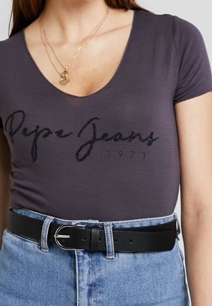 Harmaa vartalonmyötäinen v-kaula-aukkoinen t-paita, jossa musta helmikoristeinen "Pepe Jeans" -logo ja 1973-teksti, yhdistetty vaaleansinisiin korkeavyötäröisiin farkkushortseihin ja mustaan vyöhön.