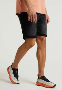Zwarte denim shorts met omgeslagen manchetten, gecombineerd met grijs en zwarte sneakers met een oranje gespikkelde zool. Eenvoudig ontwerp, casual pasvorm.