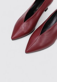 Chaussures pointues en cuir bordeaux à talons bas. Présentent un design élégant et une texture lisse, avec un détail de couture subtil le long du devant.