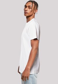 White cotton t-shirt with short sleeves and a crew neck, displayed on a model facing left, paired with light blue jeans.