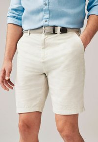 Pantaloni scurți din in gri deschis, cu un croi lejere, având buzunare laterale și un tiv care se află puțin deasupra genunchiului, asortați cu o curea țesută.