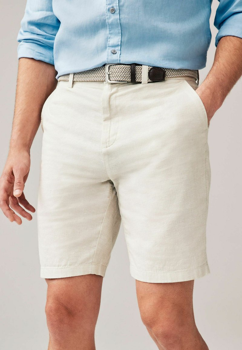 Pantaloni scurți din in gri deschis, cu un croi lejere, având buzunare laterale și un tiv care se află puțin deasupra genunchiului, asortați cu o curea țesută.