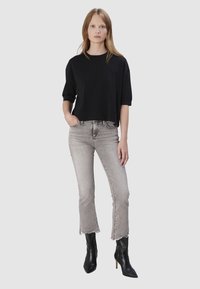 T-shirt noir cropped à manches courtes, associé à un jean gris clair taille haute avec ourlet effiloché, et des bottines noires à bouts pointus.