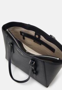 Sac fourre-tout en cuir noir avec deux poignées, intérieur en tissu beige, poche zippée intérieure et fermeture éclair argentée sur le compartiment principal.