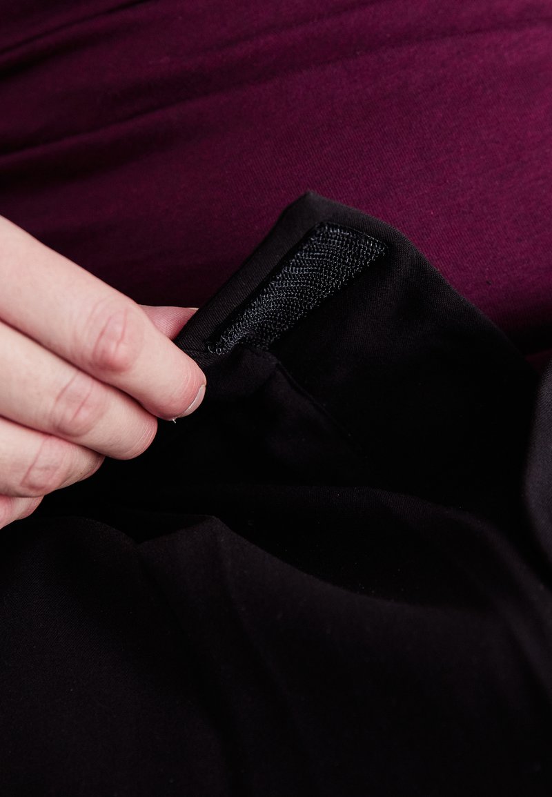 Μαύρο ύφασμα με μαλακή υφή, που διαθέτει αυτοκόλλητη επιφάνεια Velcro. Ένα χέρι ρυθμίζει το ύφασμα κοντά στην αυτοκόλλητη επιφάνεια, με φόντο σκούρο μωβ.