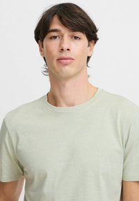 Tricou verde deschis, cu mânecă scurtă, cu un decolteu rotund, fabricat dintr-un material moale, având o croială lejeră și o textură netedă.
