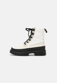 Lace-up ankle boots with a white upper, quilted texture, and a black rubber sole. Features black laces and a pull tab on the heel.