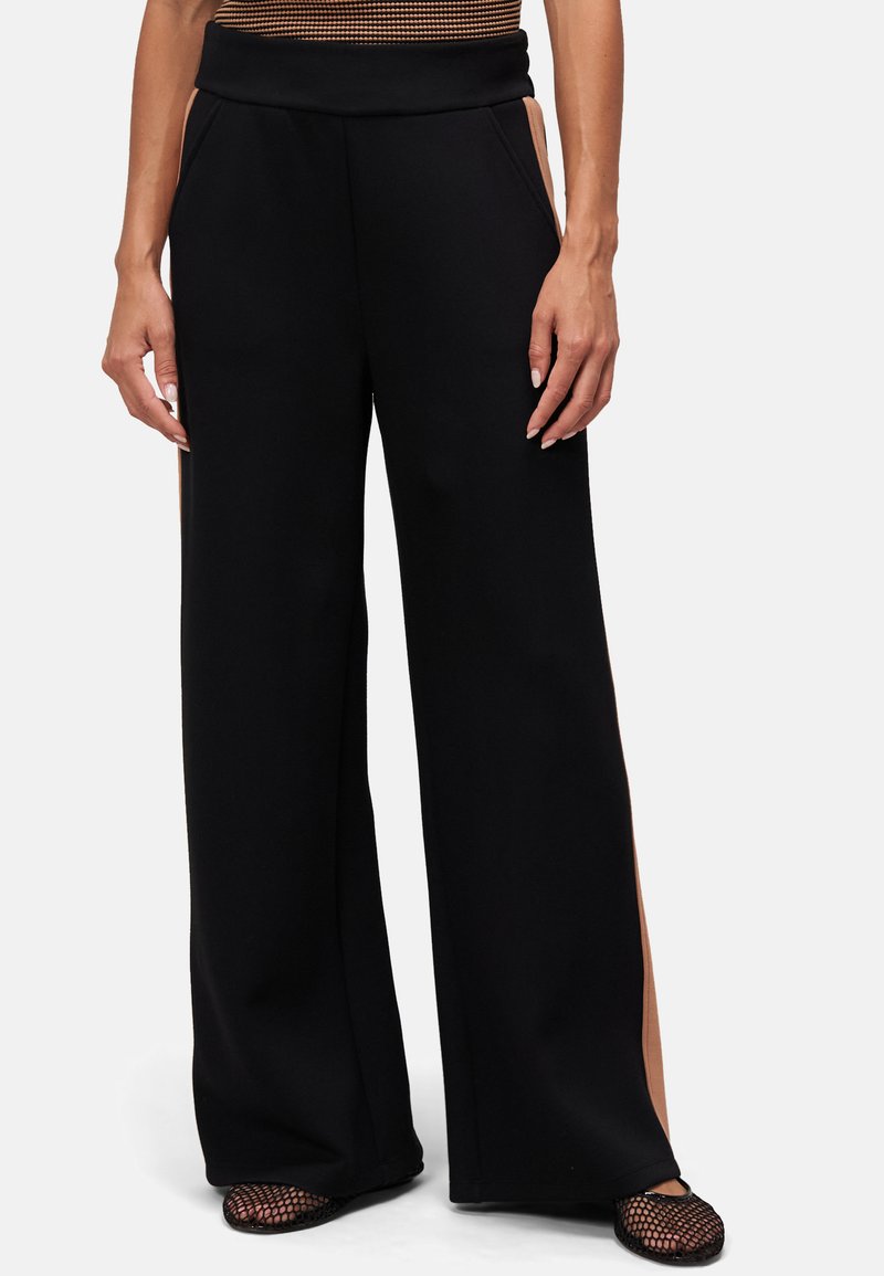 Pantalons larges noirs avec une texture lisse, dotés de fentes latérales en matériau contrastant beige, et d'une taille élastique pour le confort.