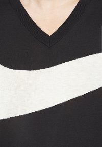 Schwarzer V-Neck-Pullover mit einem großen weißen diagonalen Streifen auf der Vorderseite, aus weichem Strickmaterial mit geripptem Halsausschnitt.