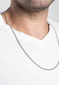 Una collana in argento metallico è appoggiata su una maglietta bianca a scollo a V, caratterizzata da un design semplice e liscio e una texture uniforme.