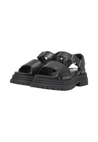 Sandales en cuir noir avec larges brides croisées et boucle ajustable. Semelle épaisse et texturée avec des rainures profondes pour une meilleure adhérence.