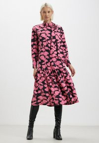 Abito a maniche lunghe con un motivo floreale rosa su sfondo nero, con vita arricciata e gonna a balze. Abbinato a stivali neri al ginocchio.