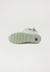 Botte en caoutchouc verte à la cheville avec une semelle texturée, ornée d'un accent de logo rouge près du talon et d'un onglet circulaire pour un enfilage facile.