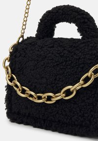 Sac à main noir texturé avec une poignée courte et une bandoulière chaîne dorée épaisse sur fond blanc.