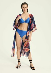 Przezroczysty kimono z kwiecistym wzorem w odcieniach czerwieni, pomarańczu i niebieskiego, nałożone na jednolity niebieski strój kąpielowy, z krótkimi rękawami i zwiewnym krojem.
