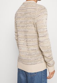 Maglione a maglia beige con un motivo testurizzato e macchie multicolori, maniche a costine e orlo. Collo rotondo e maniche lunghe.