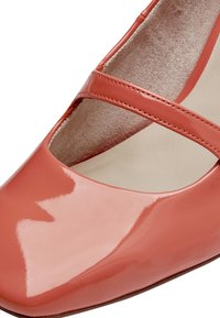 Chaussure en cuir verni corail avec un bout arrondi, une bride croisée et une doublure intérieure lisse. Elle présente une finition brillante et une silhouette structurée.